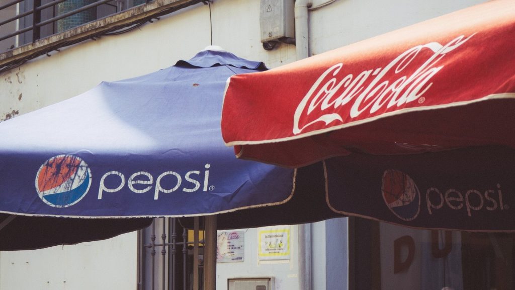 Dos parasoles: Una con el logotipo de Coca-Cola y otra con el de Pepsi
